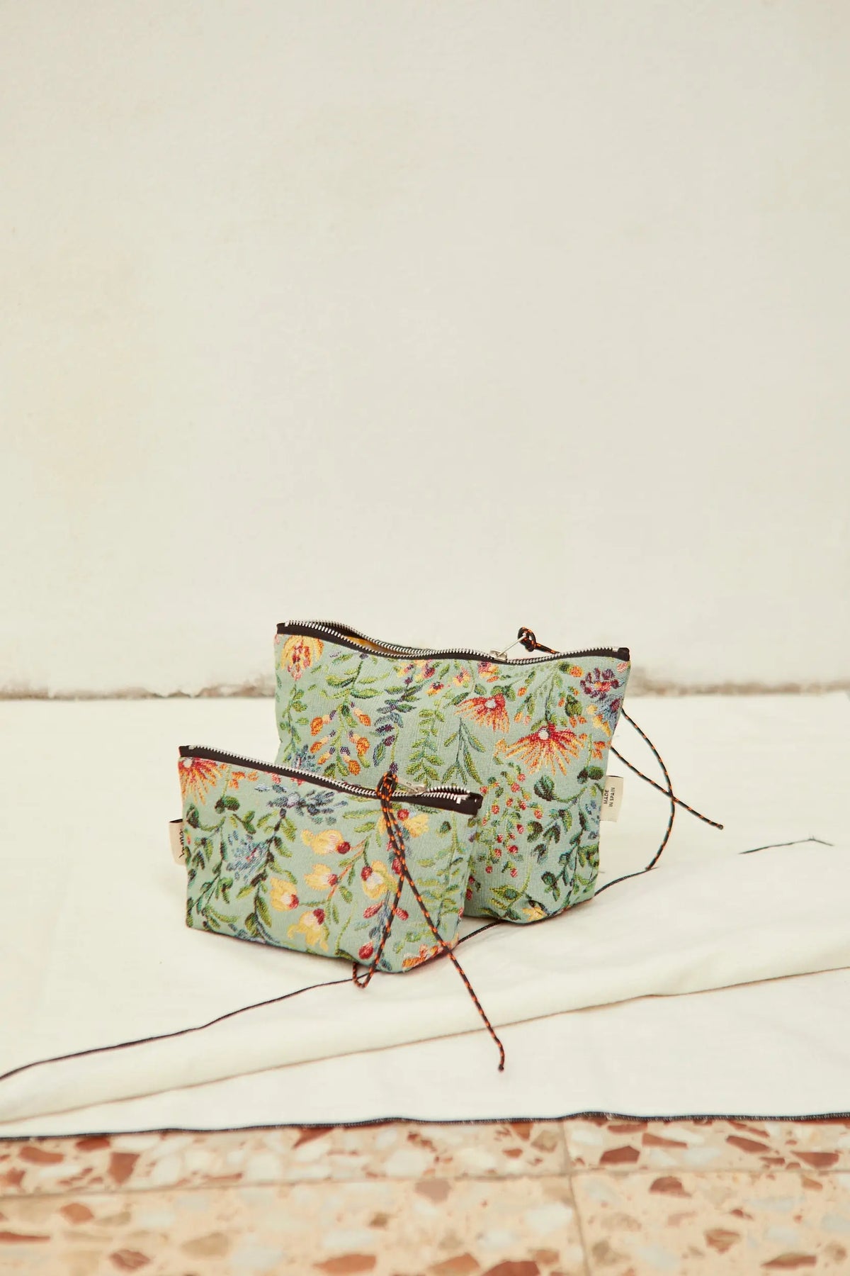 Two light blue toiletry bags with a woven floral jacquard pattern, featuring black zipper closures and cord pullers.