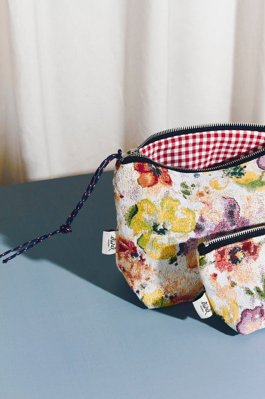 Poppy-patterned jacquard toiletry bags with red gingham lining, zipper closure, and rope pull on a blue surface.