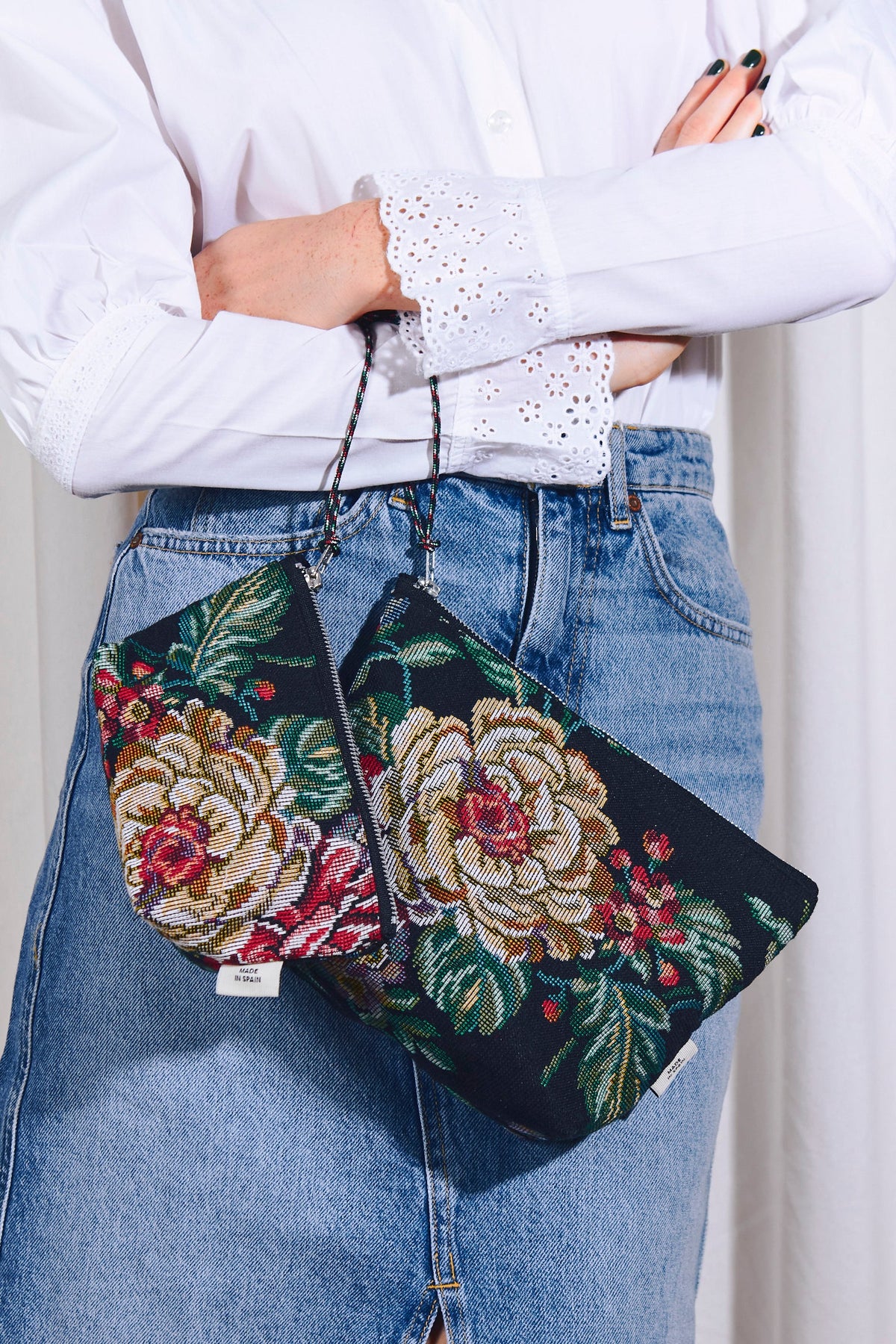 Two black jacquard zippered pouches with colorful peony patterns held against a blue denim skirt.