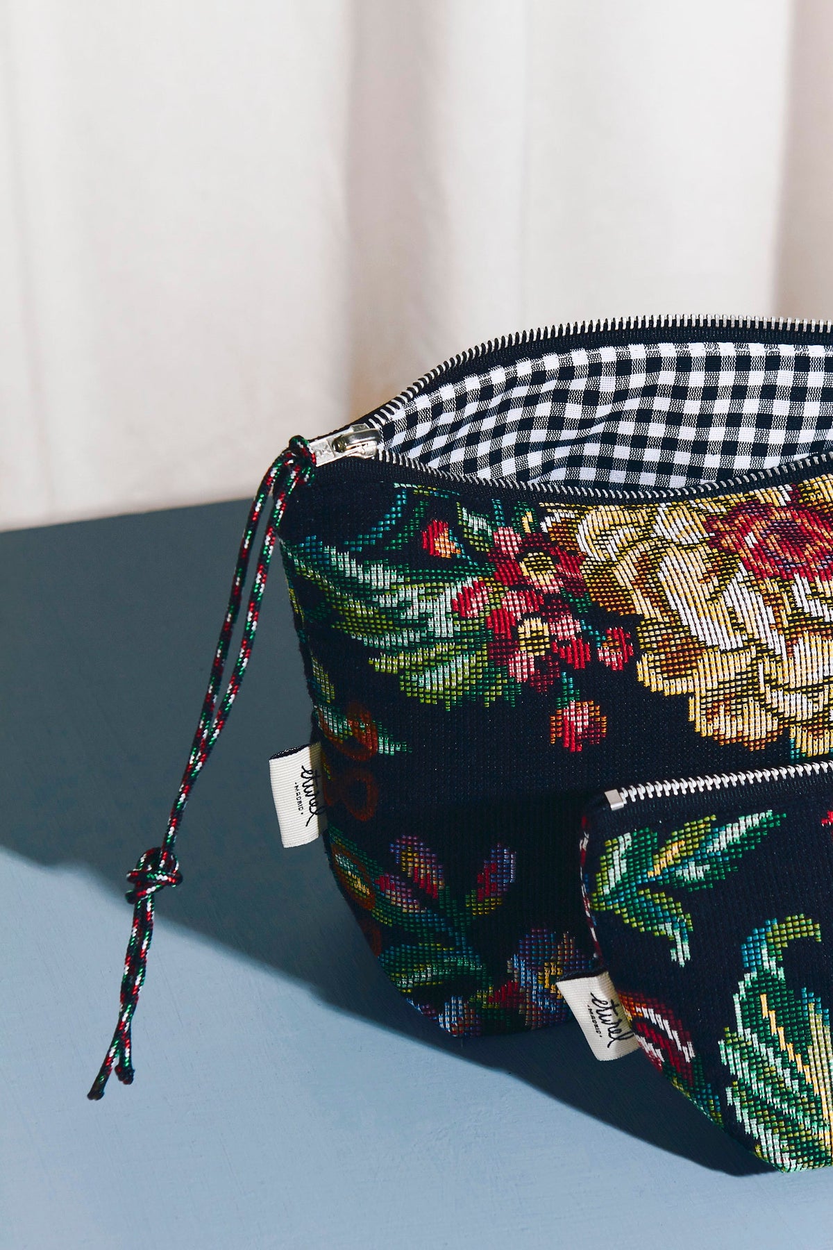 Neceser de tejido jacquard con estampado de peonías y forro de cuadros vichy blanco y negro, cierre de cremallera.