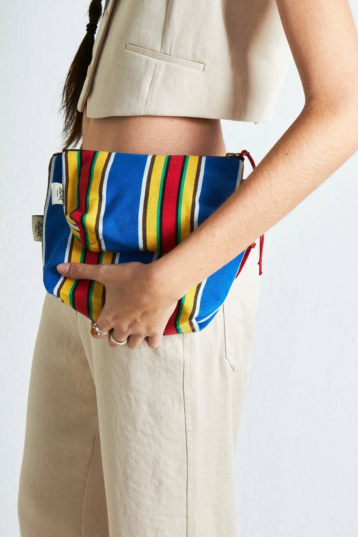 Neceser de lona con rayas verticales azules, rojas y amarillas, con cierre de cremallera y forma rectangular plana.