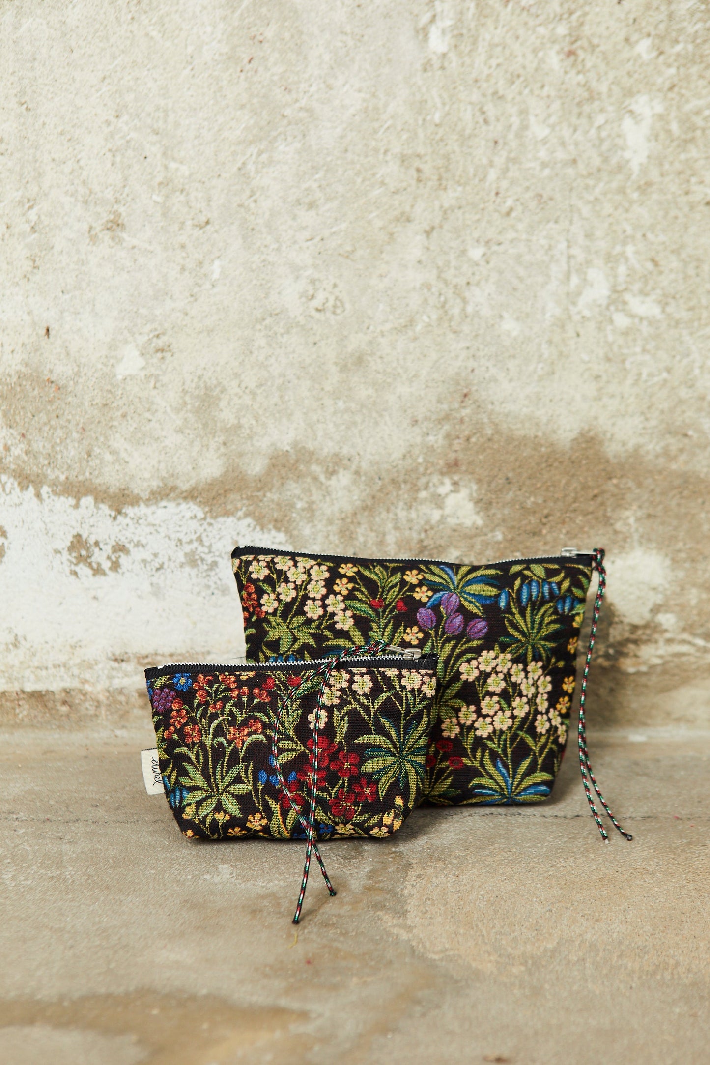 Two floral jacquard pouches in black with colorful daisy and wildflower patterns and zip closures with cord pulls.