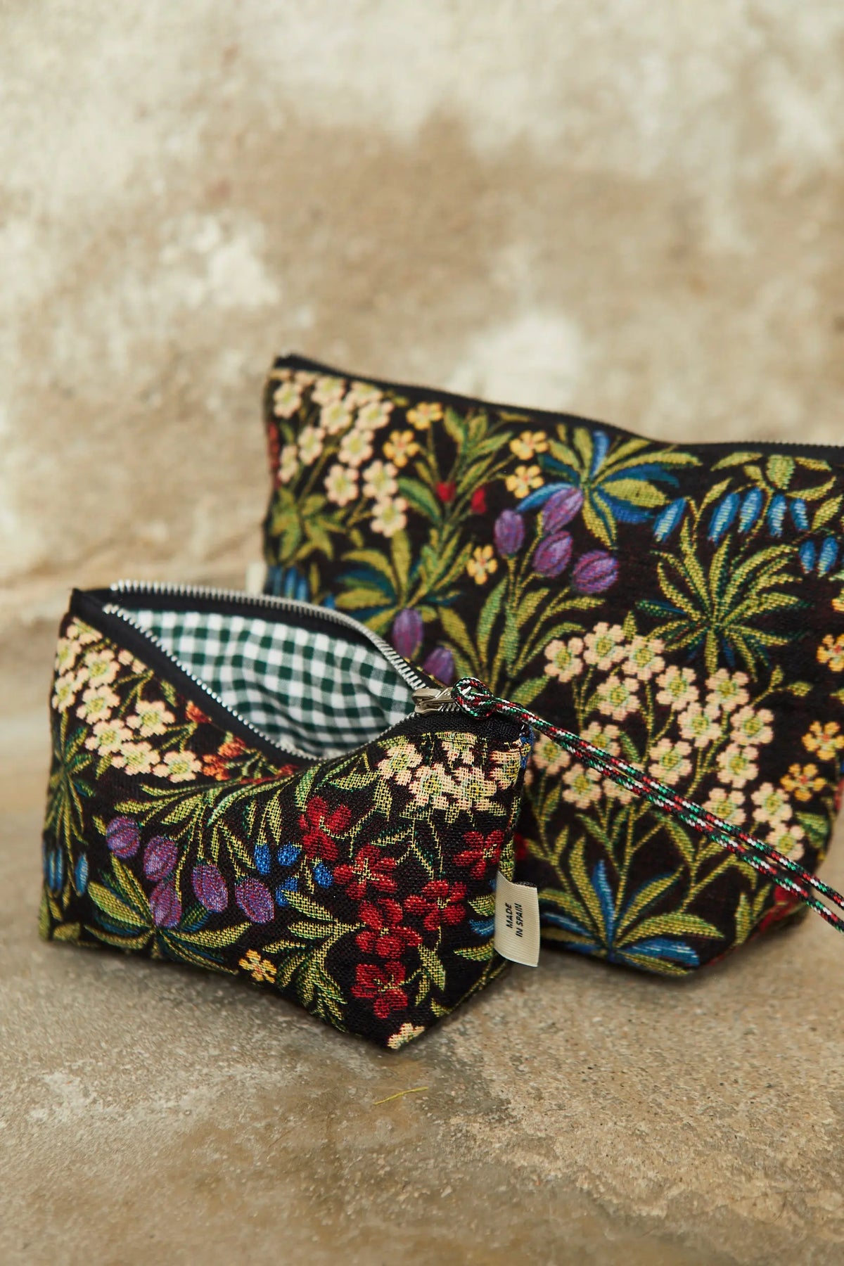 Dos neceseres de tela jacquard negra con estampado floral, flores de colores y forro interior de cuadros vichy verde.