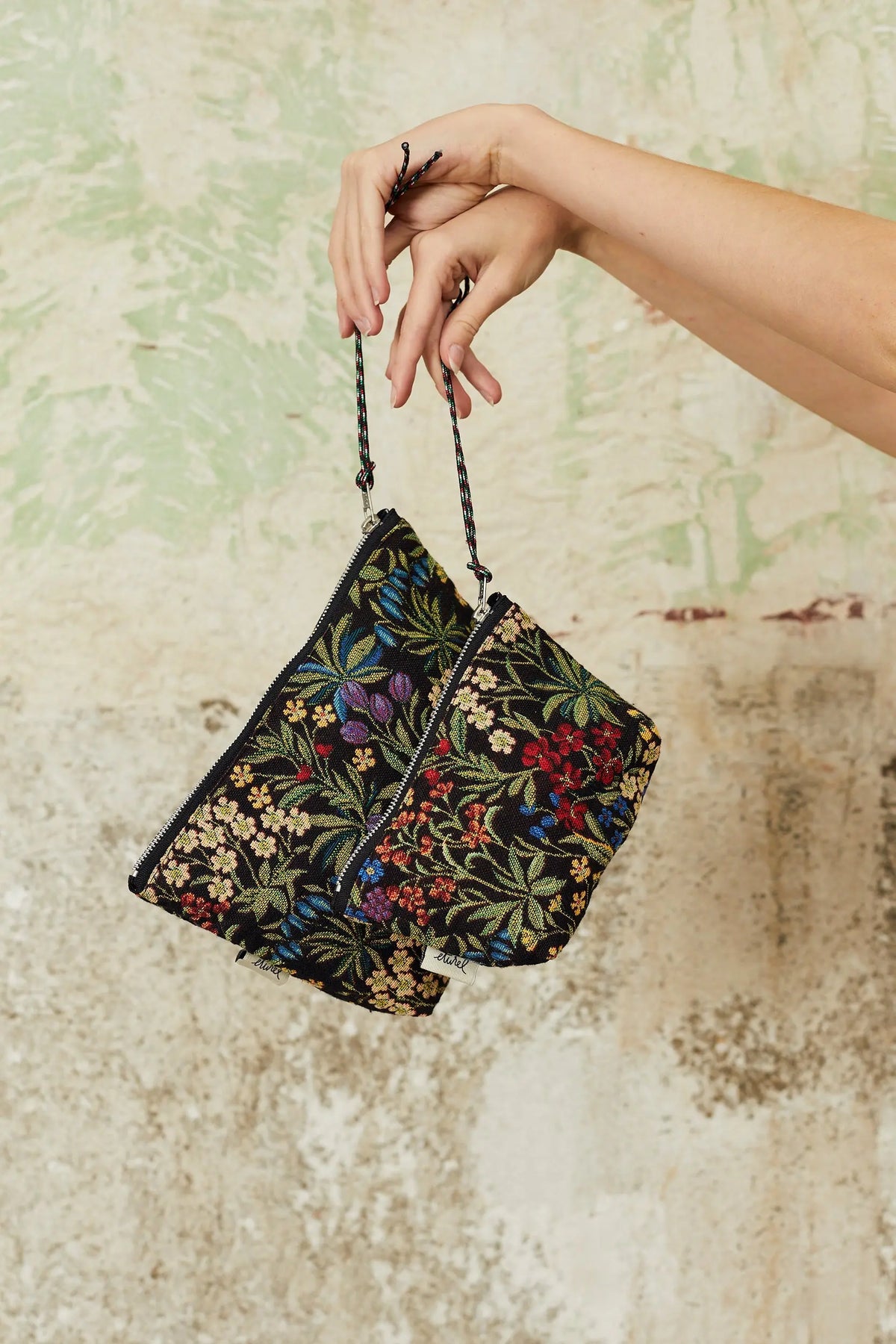 Dos neceseres de tela jacquard negra con estampado de flores coloridas, con cierre de cremallera y asa de cuerda.