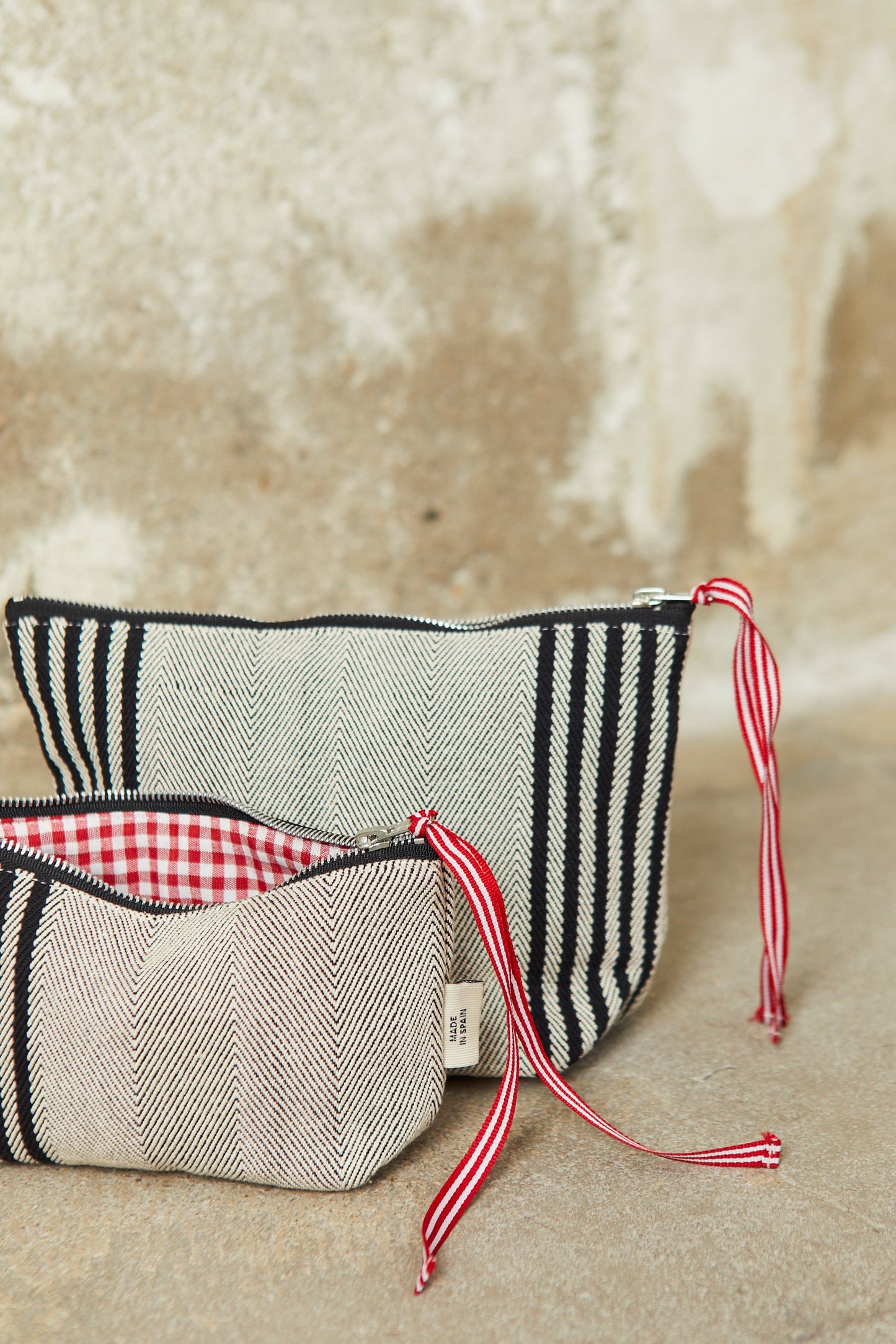 Two black and cream chevron-patterned toiletry bags with red and white striped ribbon zipper pulls and gingham lining.