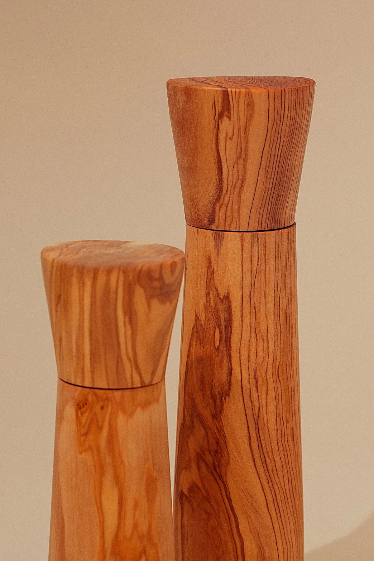 Dos molinillos de madera de olivo con veteado natural y diseño minimalista sobre fondo neutro.
