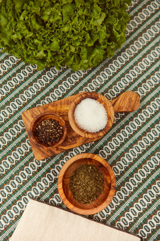 Set de cuencos de madera de olivo con especias y sal sobre una tabla rústica, vista cenital.