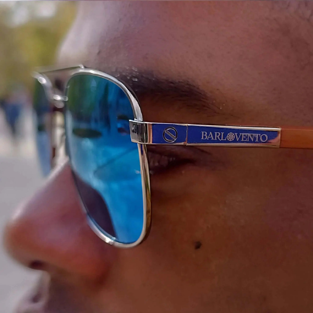 Gafas de sol estilo aviador con lentes azul reflectante, montura metálica plateada y patillas de madera natural.