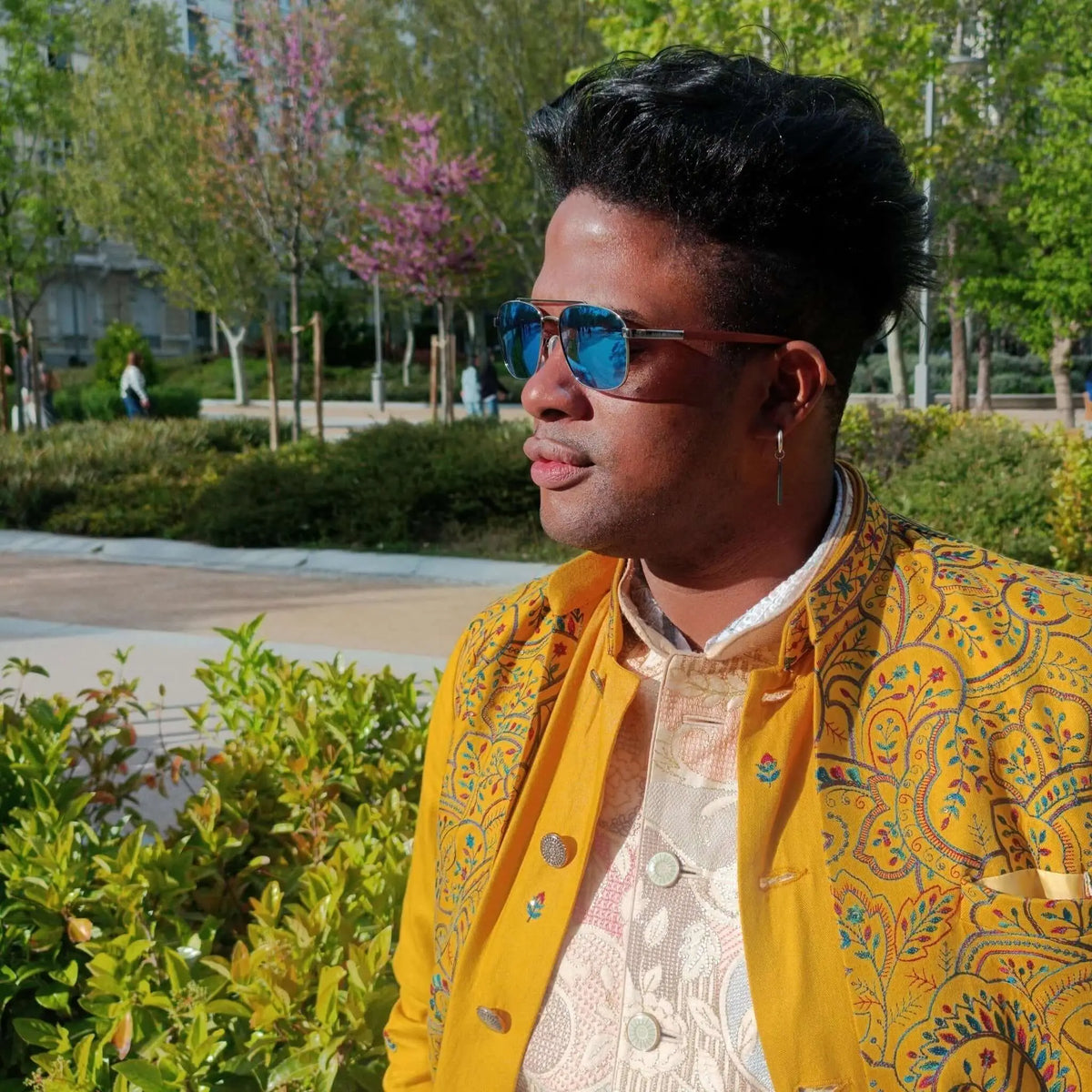 Gafas de sol estilo aviador con lentes azules y patillas de madera, lucidas por un hombre en un parque soleado.