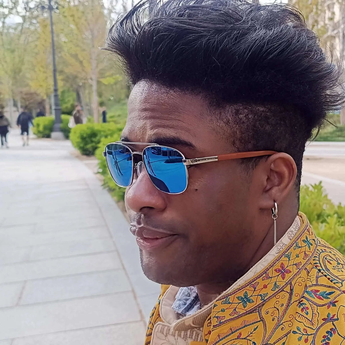 Hombre con gafas de sol aviador, lentes azules espejadas y patillas de madera, estilo elegante en entorno urbano.