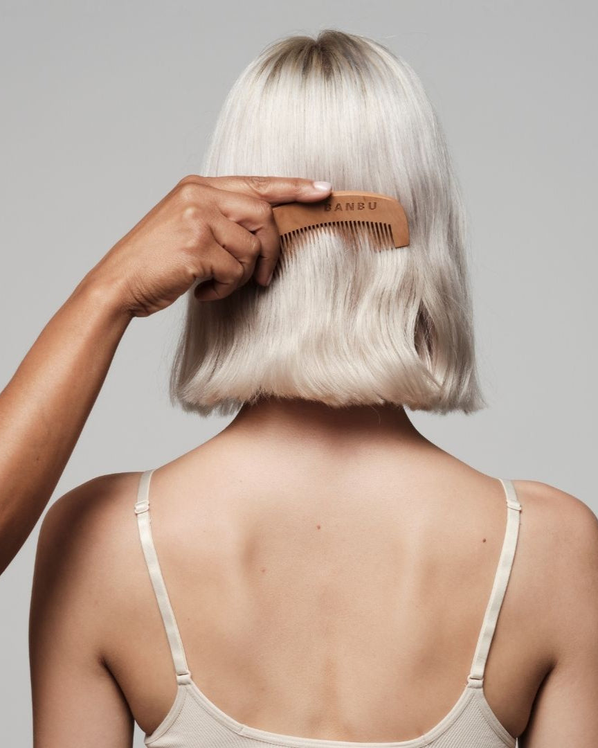 Mano usando un peine de madera natural marca BANBU para peinar el cabello rubio corto de una persona.
