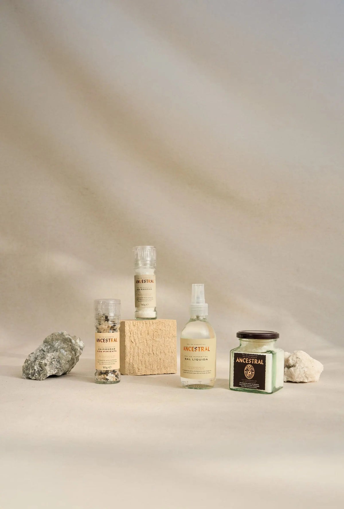 Gourmet salt collection: two grinders, a spray bottle, and a jar on a neutral background with decorative stones.