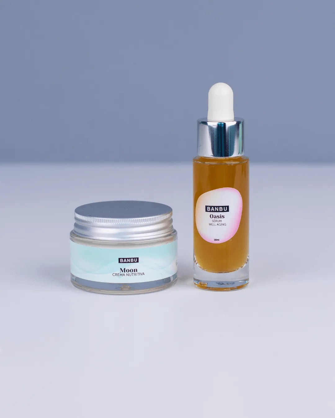 Pack Banbu: tarro de crema Moon y sérum Oasis en frasco de cristal con cuentagotas sobre fondo minimalista azul.