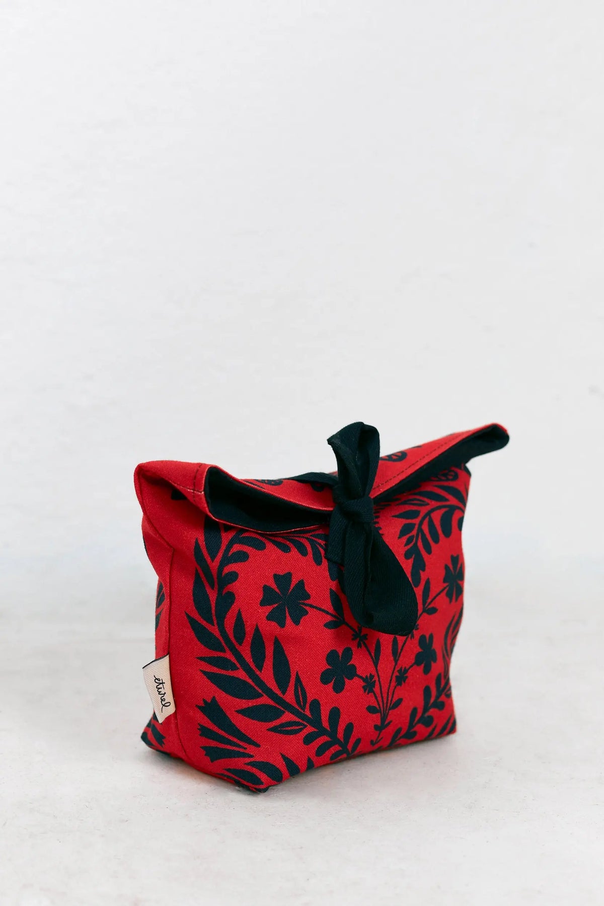 Small red fabric bread basket with black floral print and tied top closure on a white background.