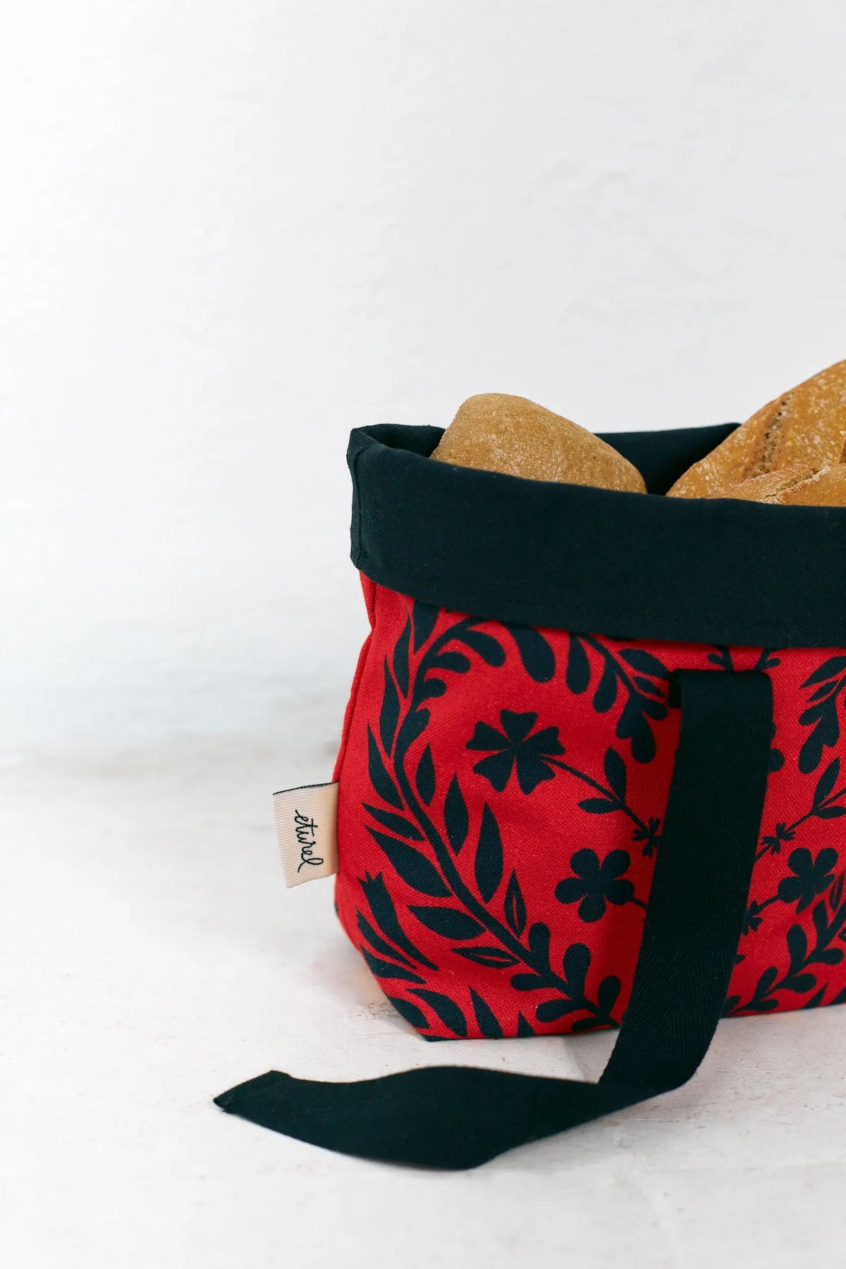 Small fabric bread basket in red with a black floral folklore pattern and solid black interior and handle.