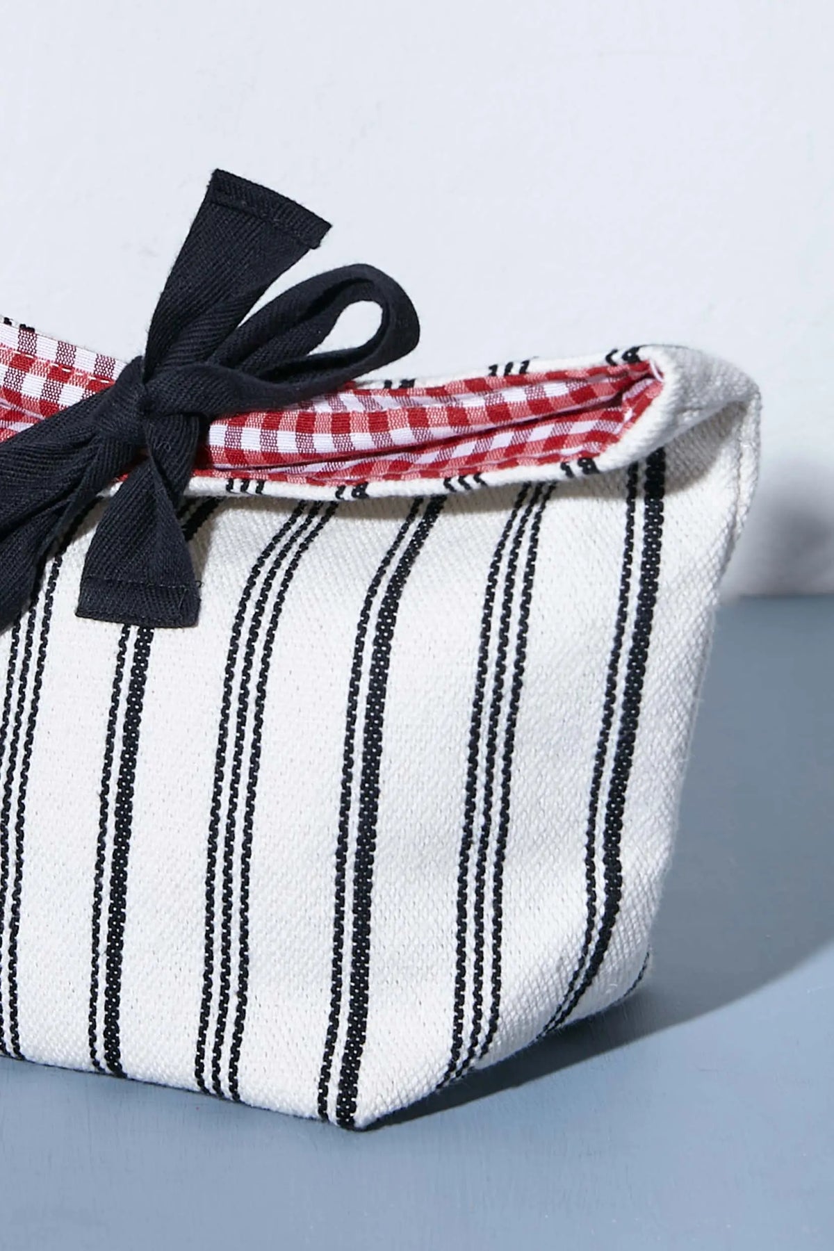 Panera de loneta con rayas negras, interior de vichy rojo y lazo negro decorativo, estilo rústico y artesanal.