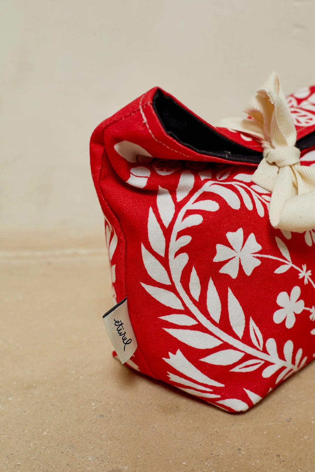 Panera de tela roja con estampado floral blanco, estilo artesanal y cierre con lazo de algodón color crema.