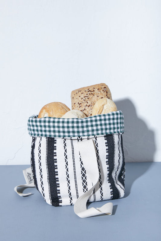 Panera de tela con estampado de rayas negras y blancas, borde interior de cuadros verdes y asas laterales, con pan.