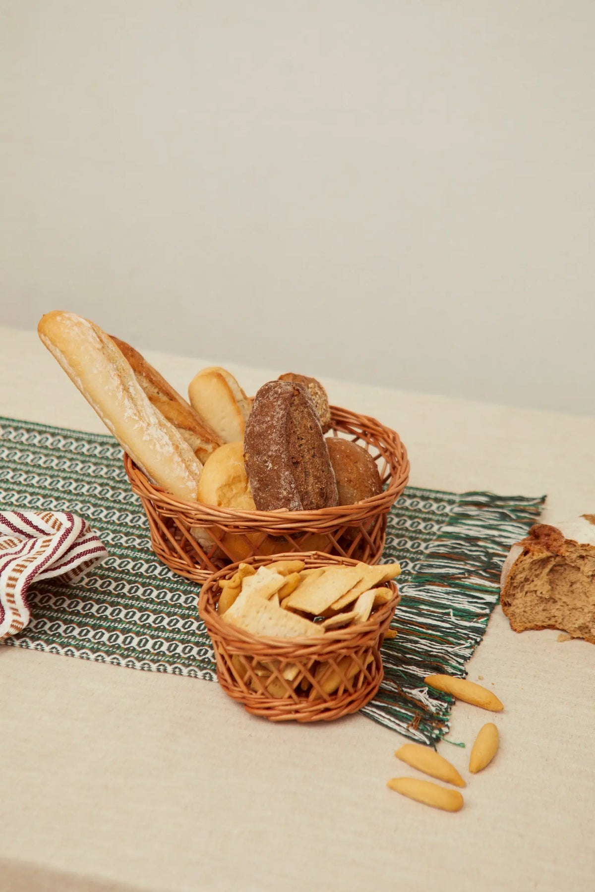 Dos paneras de mimbre natural con diseño calado, rellenas de diversos tipos de pan, sobre un camino de mesa rústico.