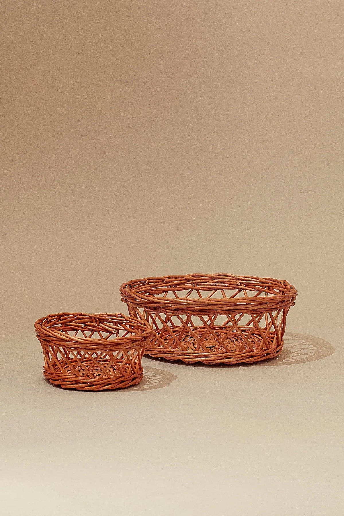 Set de dos paneras de mimbre natural con diseño calado, acabado artesanal en color marrón claro sobre fondo beige.
