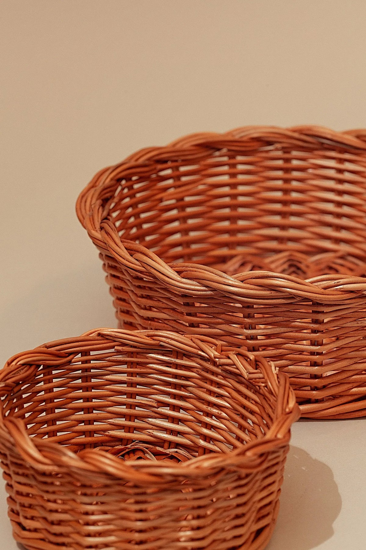 Two round, natural wicker bread baskets with a braided rim detail, presented in a warm, rustic style.