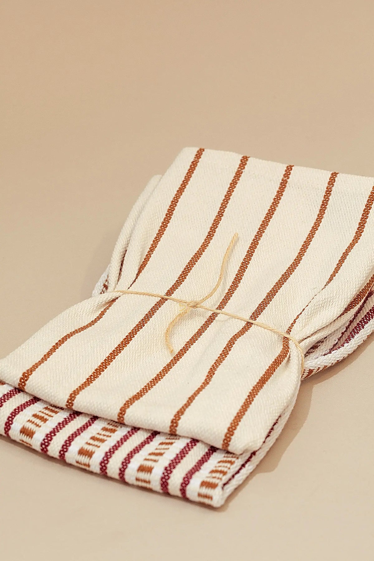 Dos paños de cocina de algodón con diseño de rayas verticales en tonos granate y crema, atados con cuerda natural.