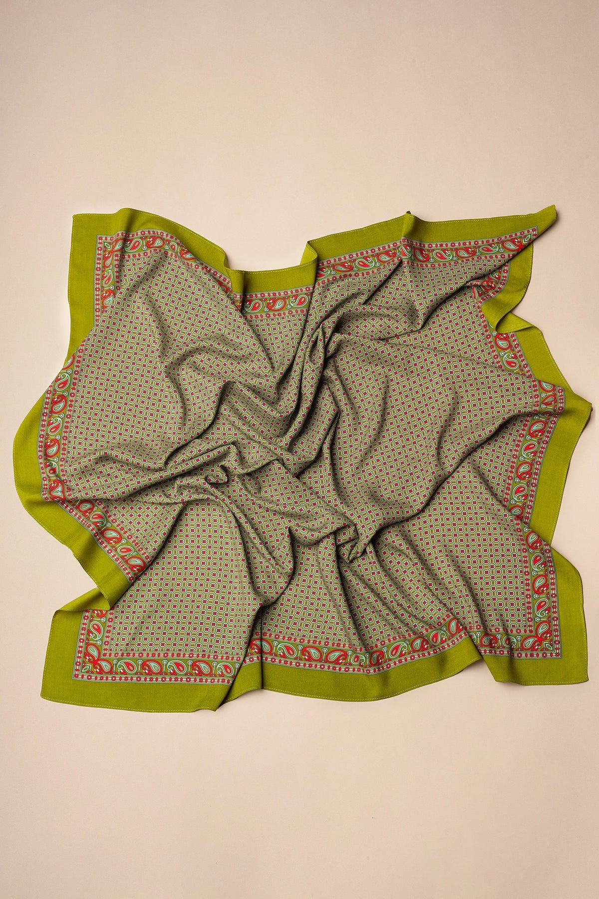 Pañuelo aragonés de tejido verde con estampado geométrico, cenefa de cachemir en tonos rojos y fondo neutro.