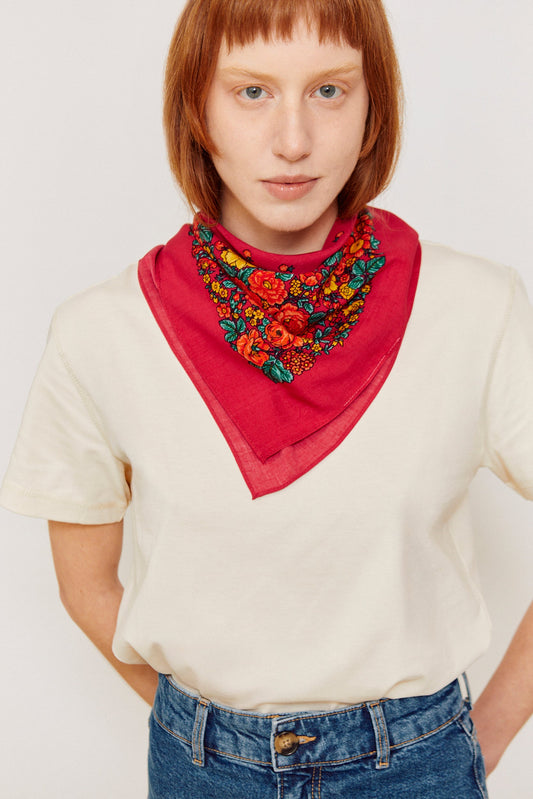 Woman wearing a pink Portuguese-style triangular bandana featuring a vibrant floral print with red, yellow, and green.