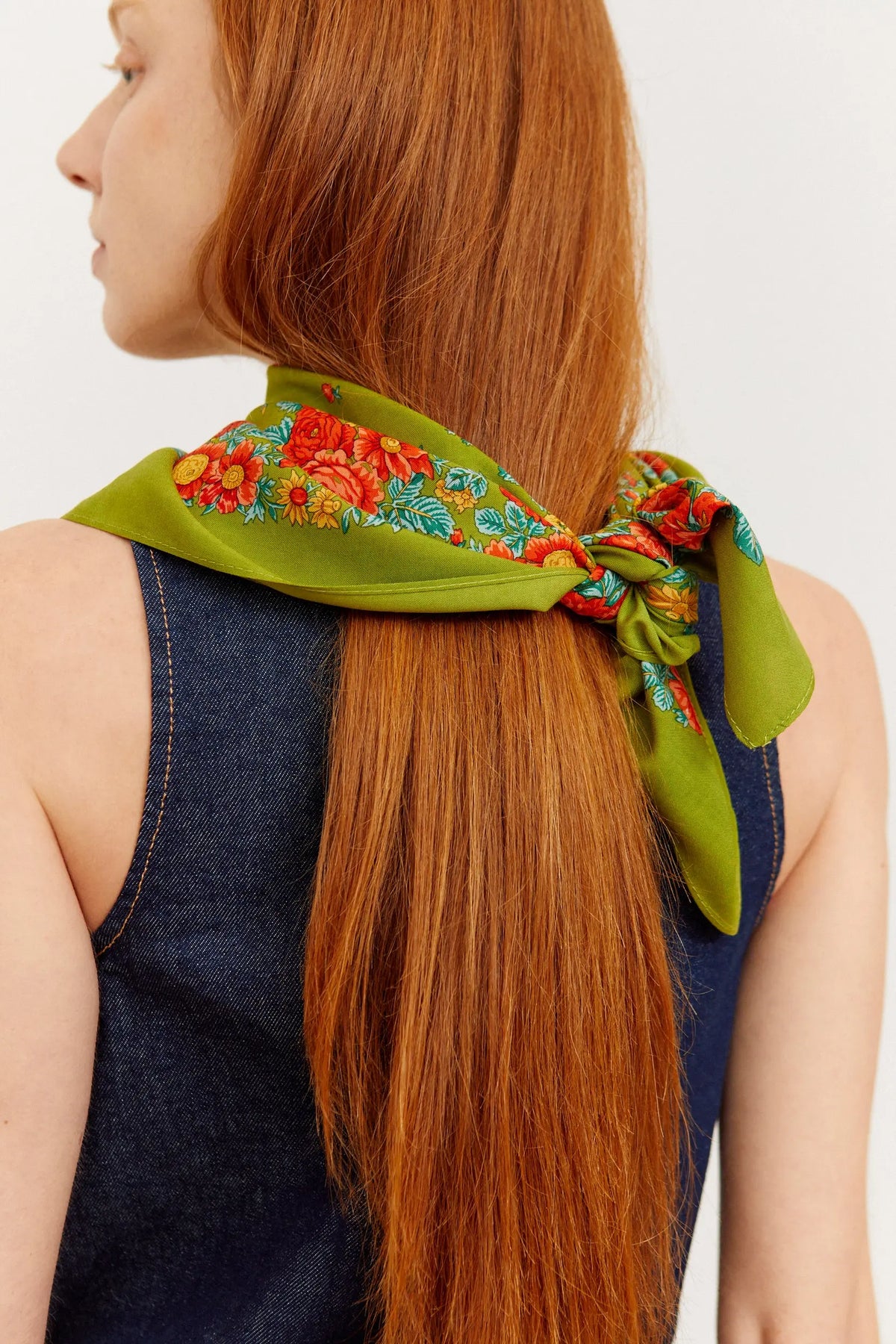 Olive green scarf with a vibrant red and orange floral border, tied neatly around a person's long auburn hair.