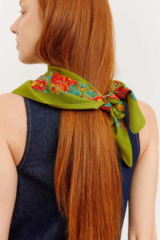 Olive green scarf with a vibrant red and orange floral border, tied neatly around a person's long auburn hair.