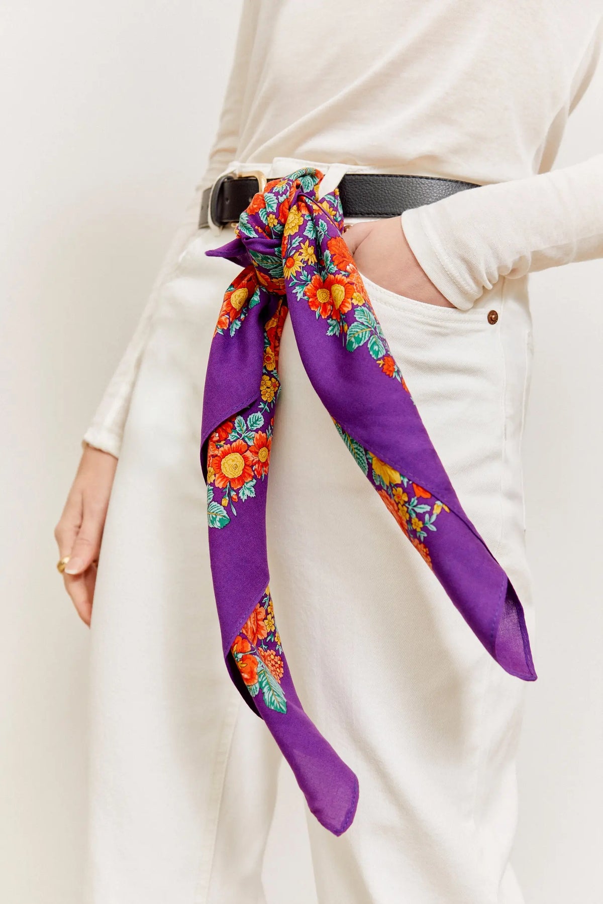 Pañuelo morado con estampado de flores coloridas estilo portugués, anudado en la cintura de pantalones blancos.