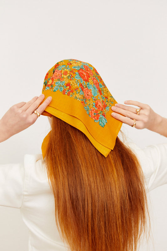 Pañuelo estilo portugués color ocre con estampado floral multicolor, colocado sobre el cabello de una mujer.