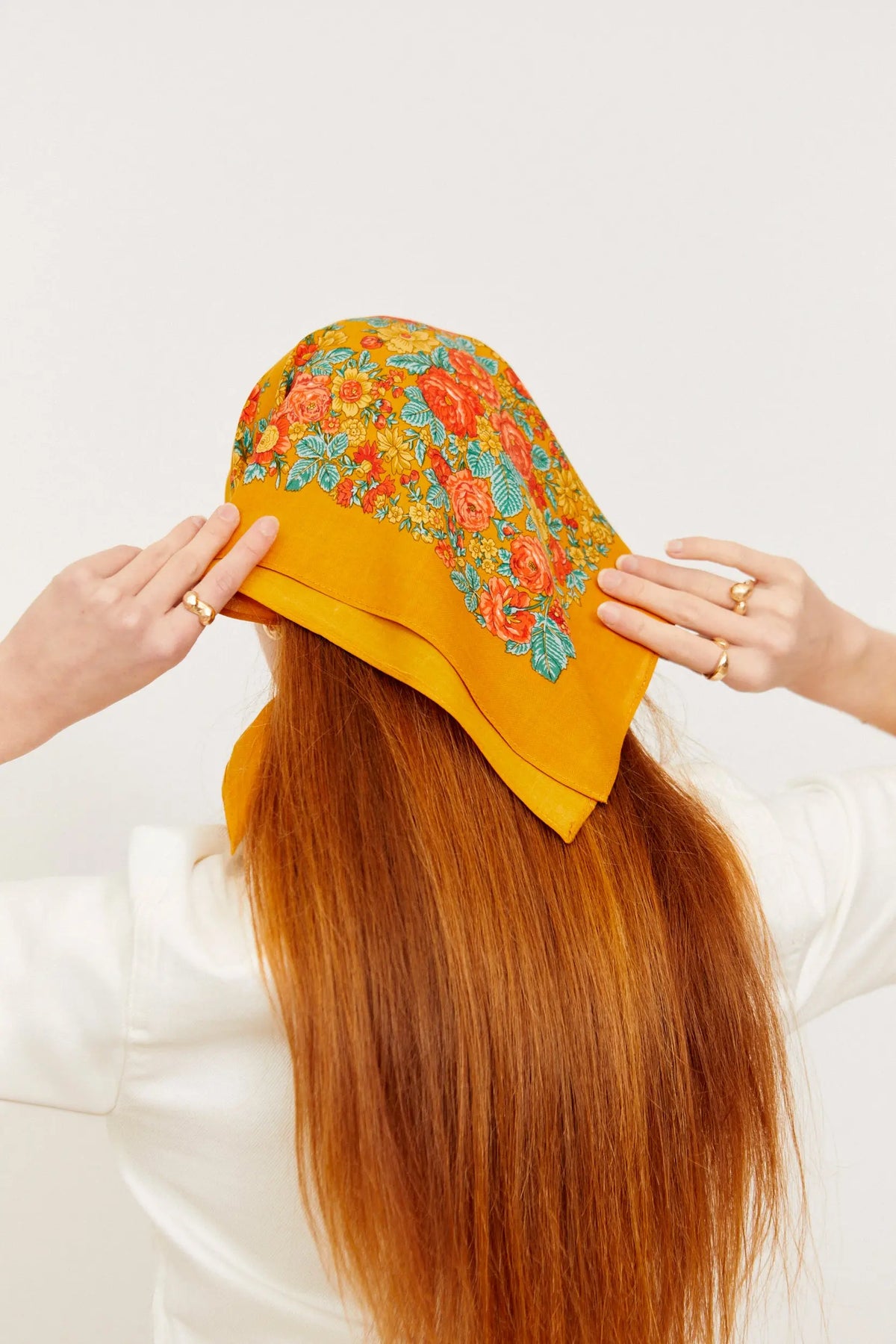 Pañuelo estilo portugués color ocre con estampado floral multicolor, colocado sobre el cabello de una mujer.