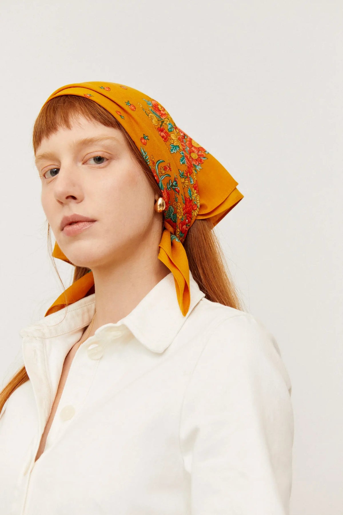 Mujer pelirroja luciendo un pañuelo ocre con estampado floral multicolor al estilo tradicional portugués.
