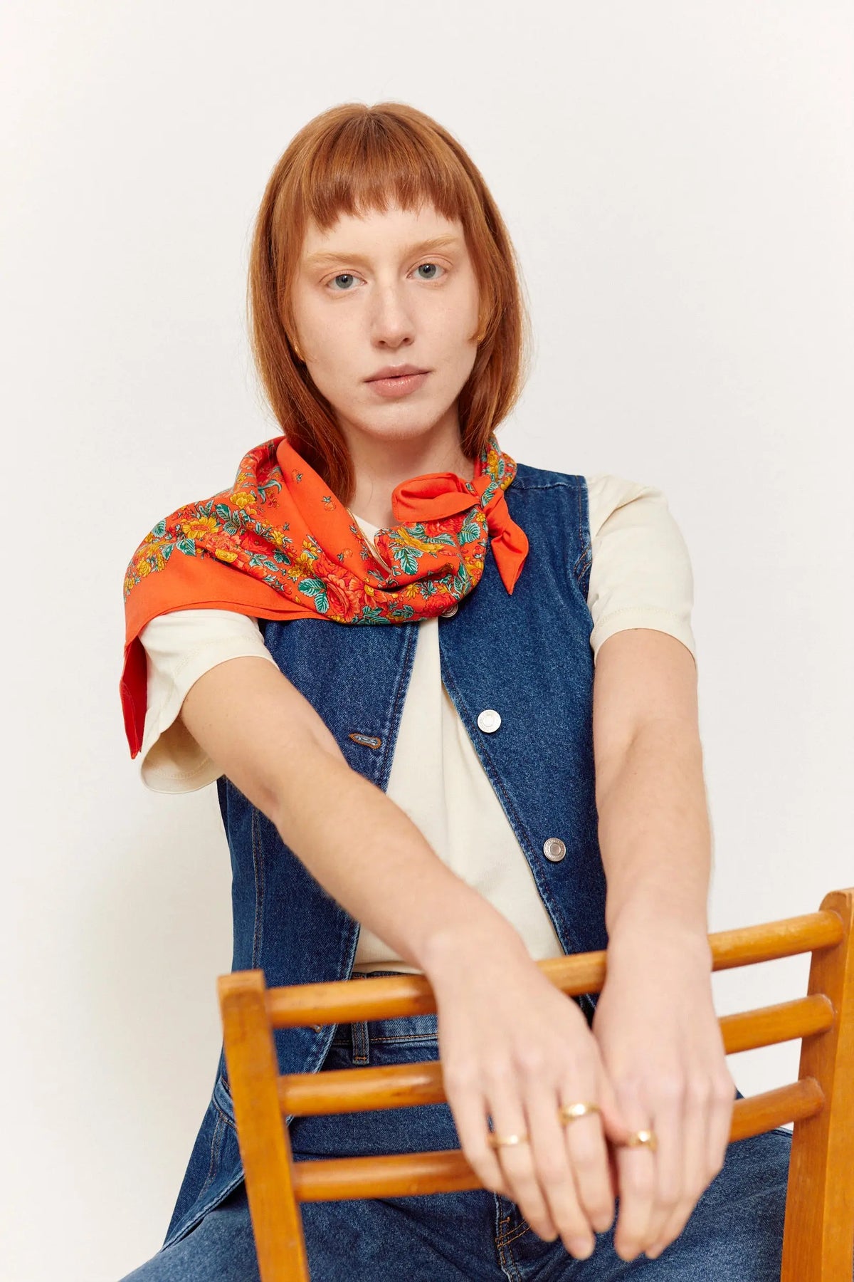 Red Portuguese-style square scarf with a vibrant floral pattern tied around the neck of a woman in a denim vest.