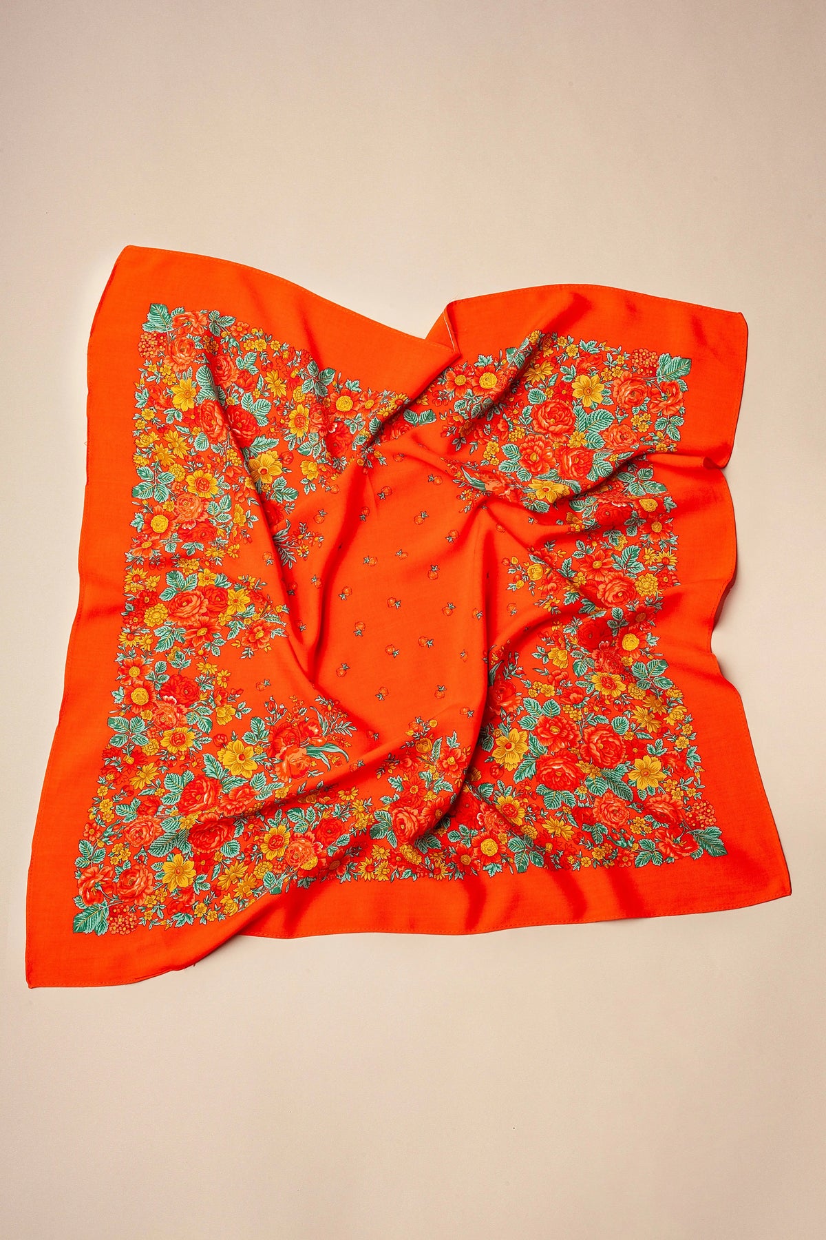 Red square scarf with a floral border featuring yellow and orange flowers and green leaves on a light background.