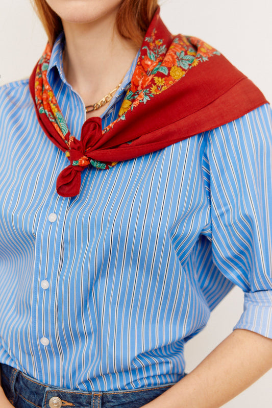 Pañuelo estilo portugués color granate con estampado de flores coloridas, anudado al cuello sobre camisa de rayas azules.