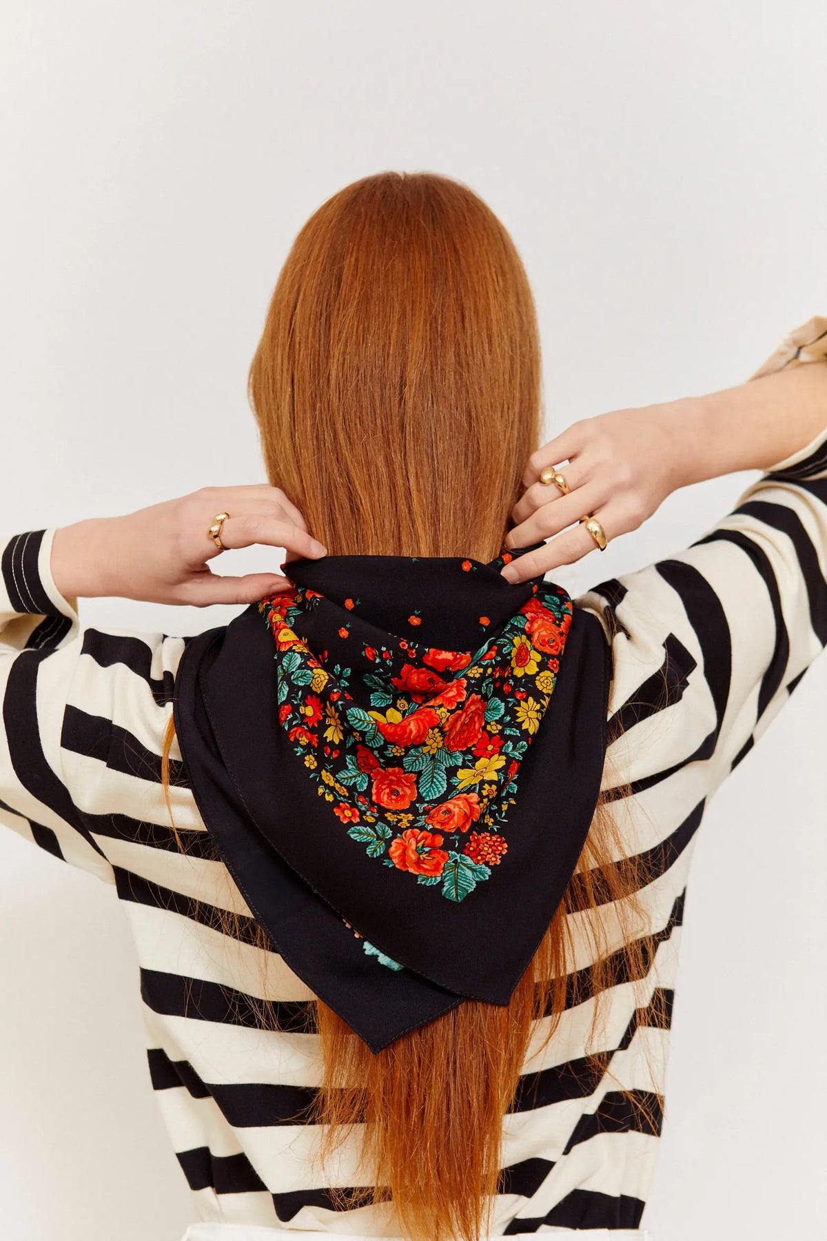 Pañuelo negro con estampado floral colorido de estilo tradicional portugués, anudado al cuello sobre una camiseta a rayas.