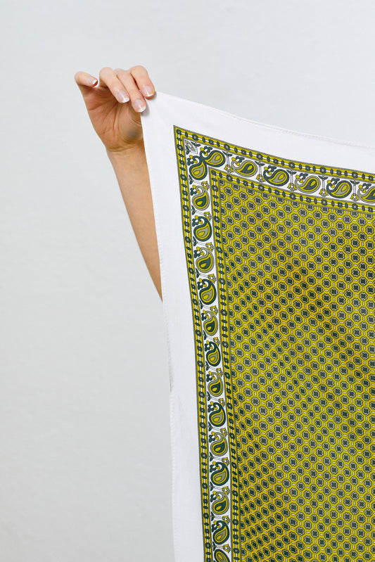 Ochre-colored handkerchief with intricate geometric and paisley-style border patterns, held up against a white background.