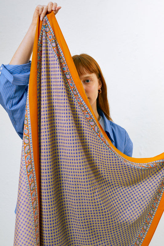 Pañuelo con estampado geométrico azul y bordes anchos en tono anaranjado con detalles de motivos vegetales.