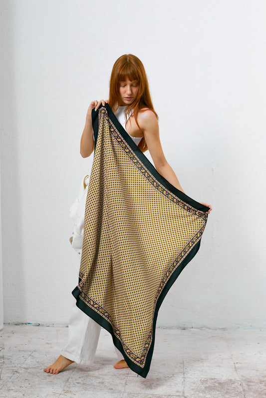 Mujer sosteniendo un pañuelo aragonés con estampado geométrico en tonos dorados y bordes negros con detalles tipo paisley.