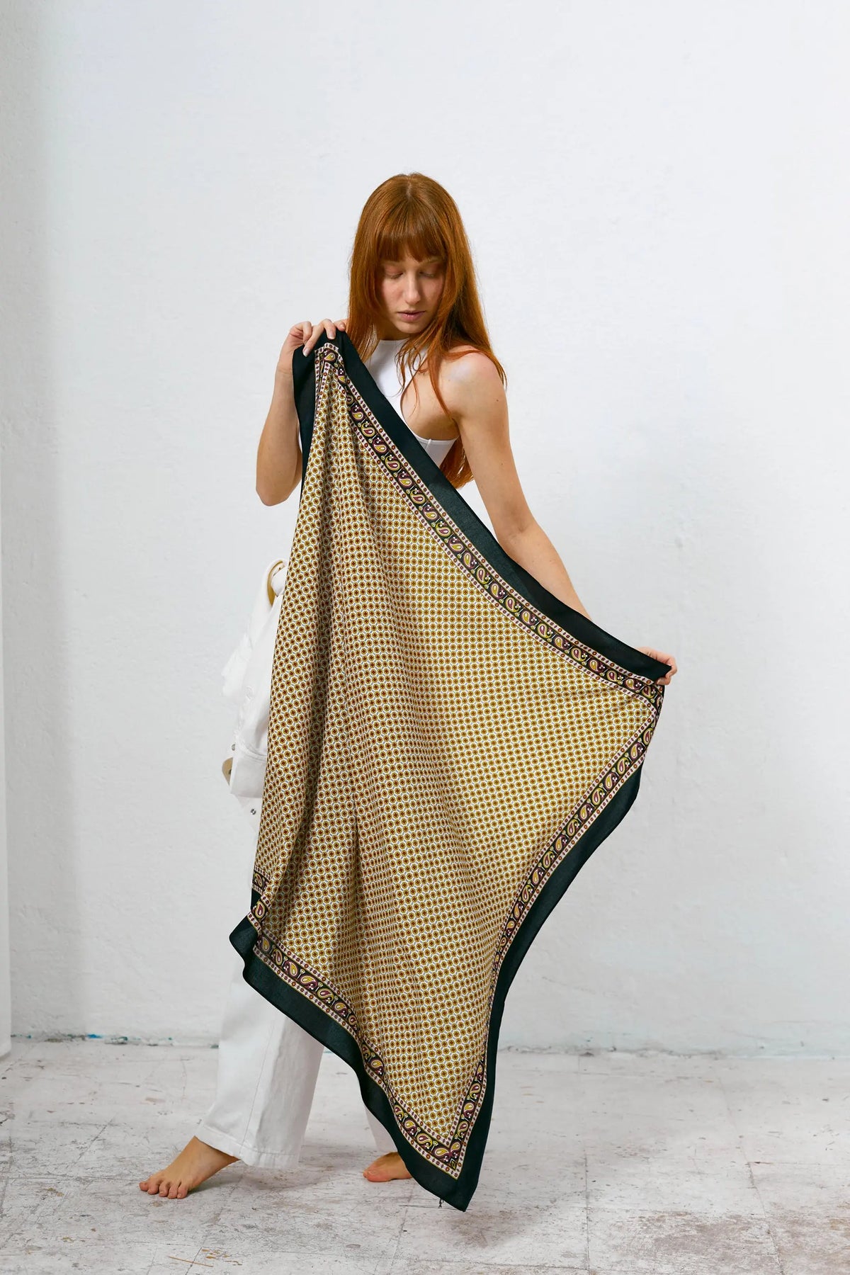 Mujer sosteniendo un pañuelo aragonés con estampado geométrico en tonos dorados y bordes negros con detalles tipo paisley.