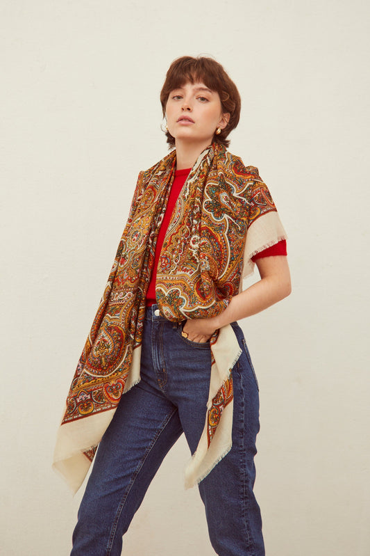 Pañuelo de lana blanco con estampado paisley multicolor y bordes deshilachados sobre modelo con camiseta roja y jeans.