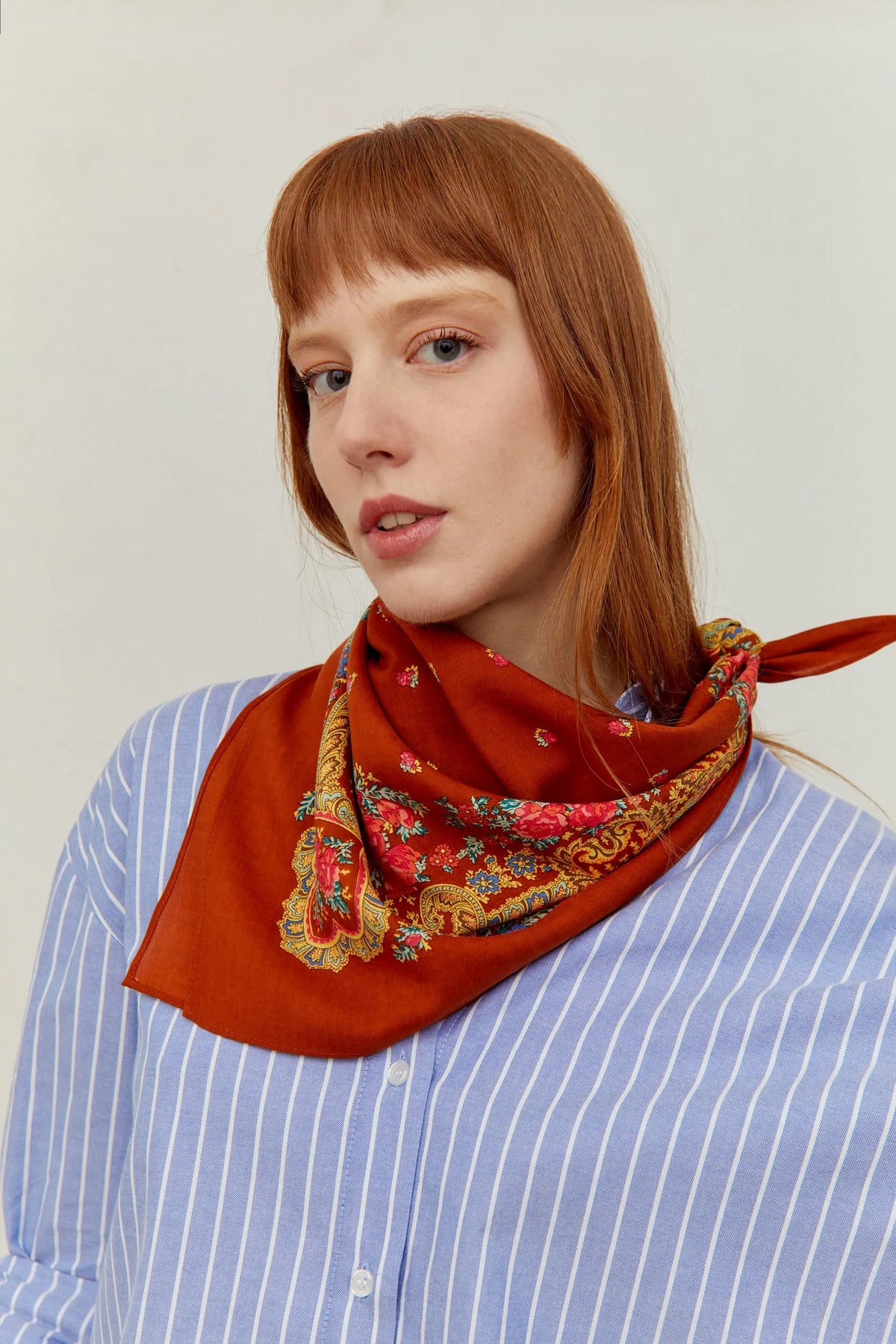 Pañuelo color caldero con estampado floral tradicional portugués y detalles de cadenas anudado al cuello.