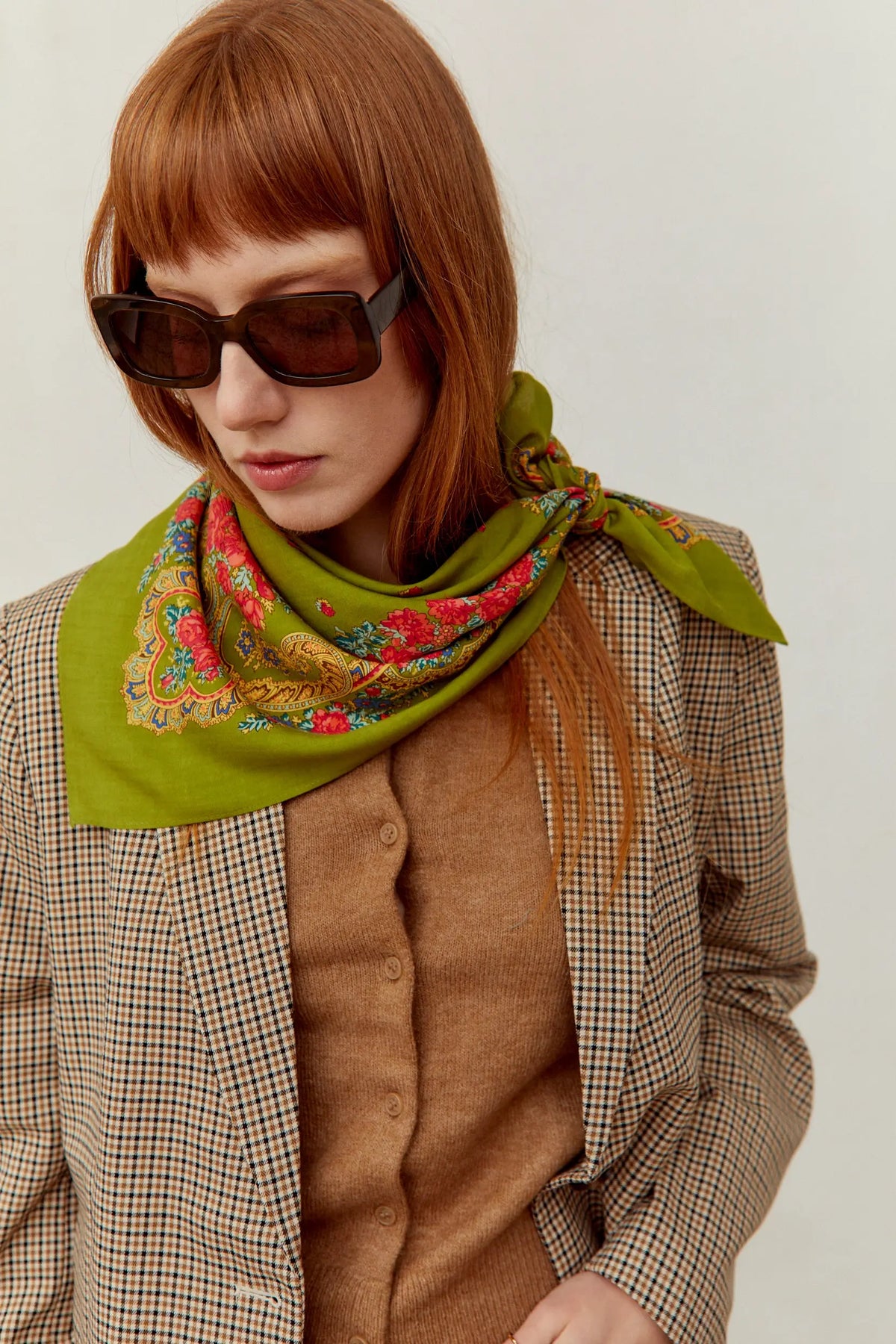 Pañuelo verde oliva con estampado floral y de cadenas, estilo clásico anudado al cuello, sobre una americana de cuadros.