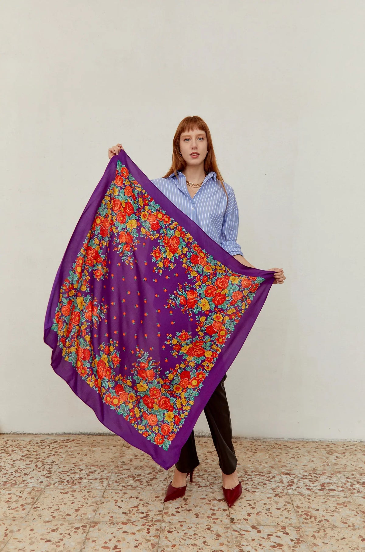 Woman holding a purple square scarf with a vibrant, multicolor floral print of red, orange, and yellow roses.
