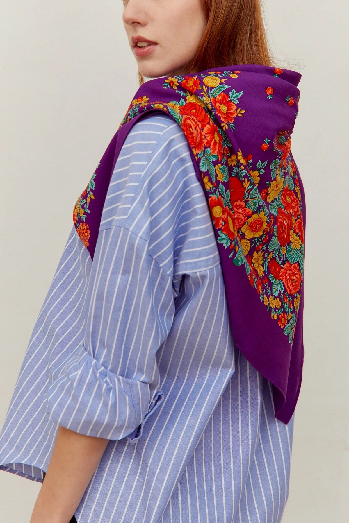 Pañuelo de estilo portugués morado con estampado de flores rojas y amarillas, sobre una camisa de rayas azules.