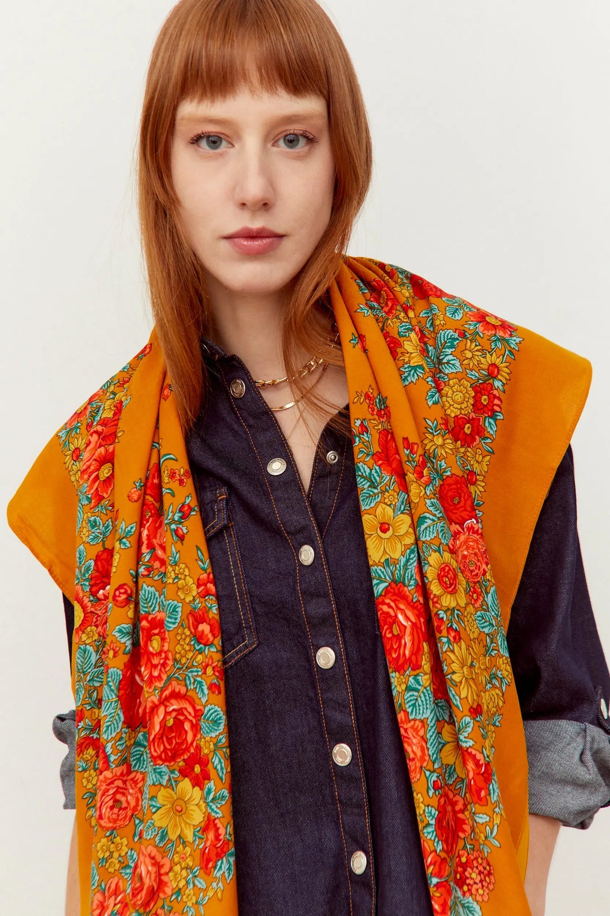 Pañuelo estilo portugués color ocre con estampado floral en tonos rojos, amarillos y hojas verdes sobre modelo.