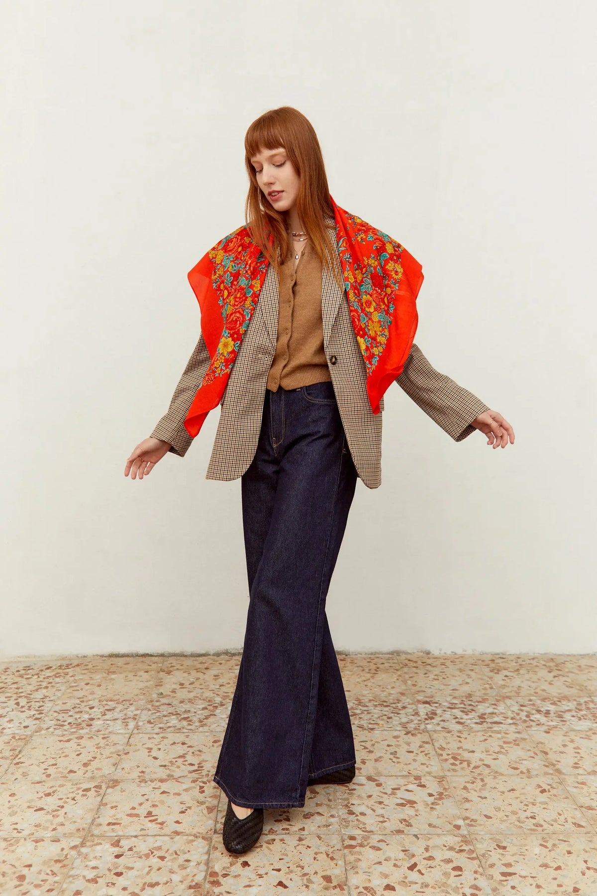Pañuelo rojo de estilo portugués con estampado de flores coloridas sobre tela ligera, usado sobre un blazer a cuadros.