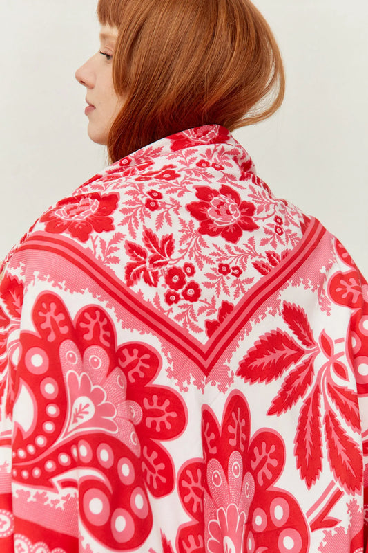 Pañuelo blanco con estampado floral y geométrico en tonos rojos y rosas, sobre los hombros de una mujer pelirroja.